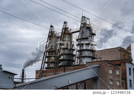 Dark smoke rises from tall smokestacks of an industrial manufacturing plant under a cloudy sky, showcasing the facility's emissions and activity 123496536