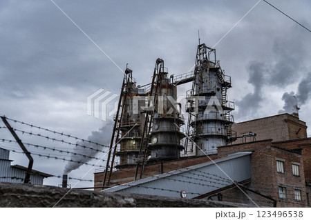 Thick smoke is released from the tall smokestacks of an industrial facility, indicating ongoing production. The sky is overcast, adding to the somber atmosphere 123496538
