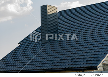 A sleek and modern roof features black metal tiles that reflect sunlight, highlighting the contemporary design of the house and its chimney structure A sleek and modern roof features black metal tiles that reflect sunlight, highlighting the contemporary design of the house and its chimney structure 123496548
