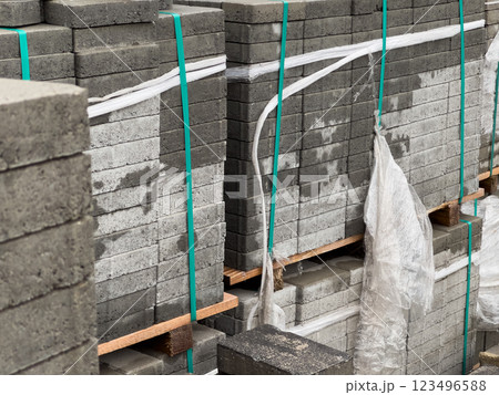 Stacks of cobblestones are securely bound together on pallets, ready for sidewalk installation in a bustling urban environment during the early hours of the day 123496588