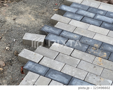 Workers are carefully laying down paving stones on a gravel foundation, progressing through the pavement repair project in this residential neighborhood 123496602