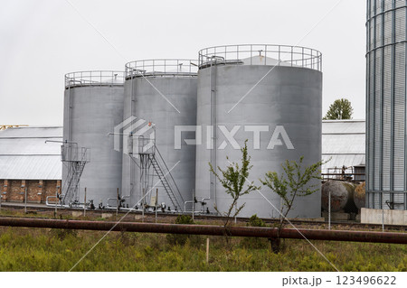 Three large gray storage tanks are situated in an industrial area, complete with metal catwalks and ladders, indicating a functional facility 123496622