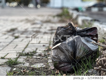 A black plastic bag overflowing with trash rests on the ground next to a brick walkway, highlighting the litter problem in a neglected public space A black plastic bag overflowing with trash rests on the ground next to a brick walkway, highlighting the litter problem in a neglected public space 123496638