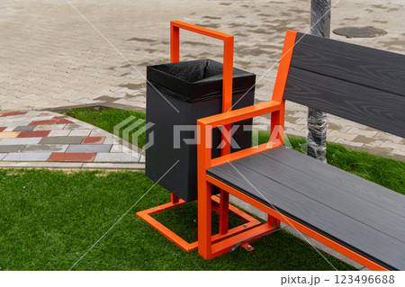 A contemporary garbage container is mounted alongside a park bench, offering a practical solution for waste disposal in a well-maintained green space A contemporary garbage container is mounted alongside a park bench, offering a practical solution for waste disposal in a well-maintained green space 123496688