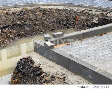 Workers are in the process of laying new pavement near a construction site where drainage problems have created a muddy area and exposed soil around the edges 123496714