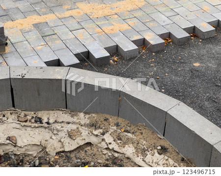 Workers are busy laying down paving stones in a construction area, where the bricks are neatly arranged, and sand is scattered nearby for leveling purposes 123496715