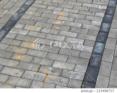 A gray brick pavement with black stripes. There is some dirt and debris on the bricks 123496717