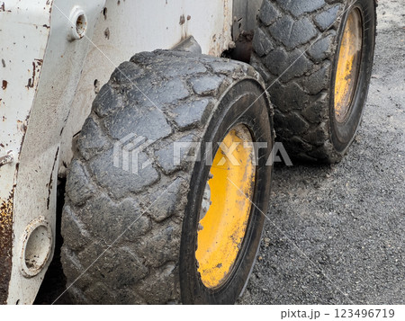 The heavy-duty tires of a bobcat are covered in mud, highlighting their use in a construction environment. The ground is gravelly and worn from activity throughout the day 123496719