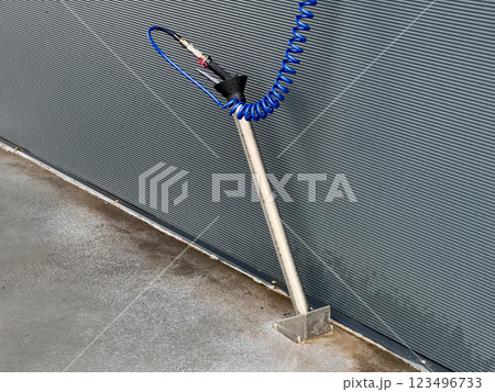 A high-pressure car washing gun is securely mounted on a stand, with a blue hose coiling to maintain readiness for effective vehicle cleaning 123496733