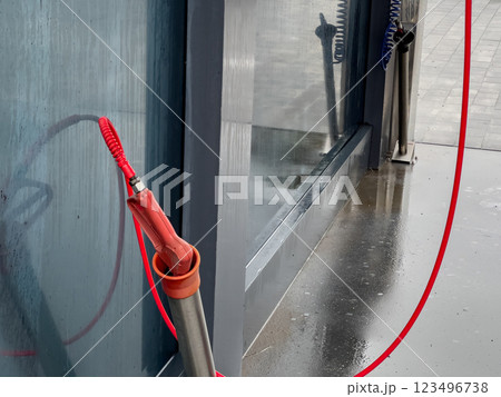 A high-pressure car washer gun stands ready for use at a self-service washing station, with droplets of water still glistening on the surface nearby A high-pressure car washer gun stands ready for use at a self-service washing station, with droplets of water still glistening on the surface nearby 123496738