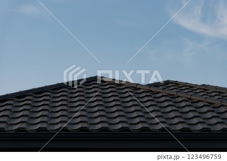 A house features a modern roof made of metal tiles, illustrating current design trends. The clear blue sky complements the sleek appearance of the roofing structure 123496759