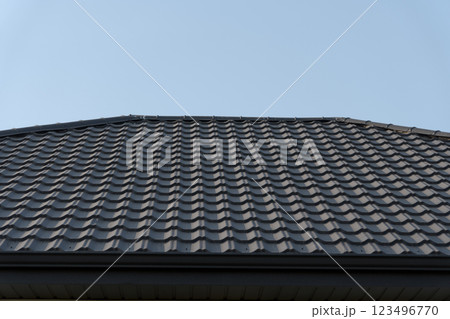 The meticulously installed metal roof tiles reflect the sunlight, creating a stunning juxtaposition against the expansive blue sky above, highlighting craftsmanship and durability 123496770