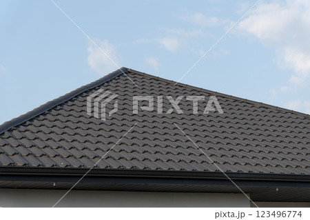 A striking rooftop features intricately arranged metallic tiles, glimmering under the warm sunlight, providing a stylish touch to the structure, set against a serene blue backdrop A striking rooftop features intricately arranged metallic tiles, glimmering under the warm sunlight, providing a stylish touch to the structure, set against a serene blue backdrop 123496774