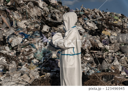 Dressed in a protective suit, the worker surveys the expansive landfill filled with discarded items, emphasizing the urgent need for sustainable waste management initiatives 123496945
