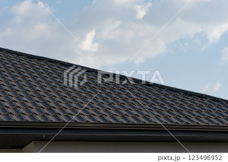 Under a bright sky, a meticulously crafted metal tile roof captures the light, reflecting both beauty and durability in a tranquil suburban neighborhood 123496952