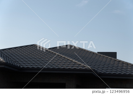 A striking view of a metal-tiled roof shines brightly against the backdrop of a clear blue sky. The architecture exudes modern charm in a peaceful suburban setting 123496956