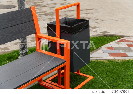The striking orange bench designed with an attached black trash bin offers convenience for park visitors, enhancing the outdoor experience in a lively setting 123497001
