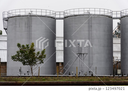 Several large fuel storage tanks stand at an industrial site, surrounded by a few trees and equipment, reflecting an overcast atmosphere in the morning light 123497021