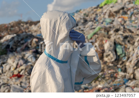 Wearing protective gear, an environmental health worker surveys a landfill overflowing with plastic waste 123497057