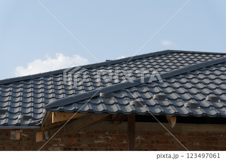 A skilled worker meticulously installs a black tiled roof atop a newly constructed home A skilled worker meticulously installs a black tiled roof atop a newly constructed home 123497061