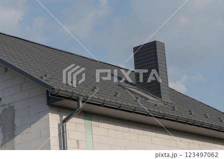 A modern roof showcases sleek shingles and a contemporary chimney against a blue sky, indicating recent construction work. The contrasting textures highlight excellent craftsmanship 123497062