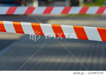 Caution tape stretches across a pathway, creating a vibrant barrier that signals restricted access. Sunlight shines brightly, illuminating the bold orange and white stripes, enhancing visibility 123497278