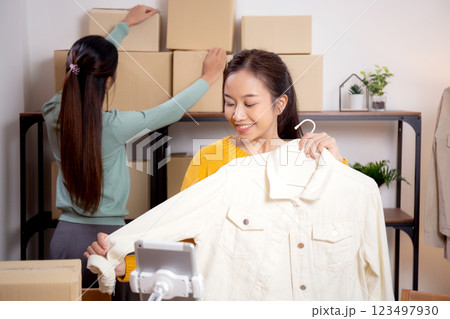 Two young asian woman live online clothing store while showing clothing with tablet on social. 123497930