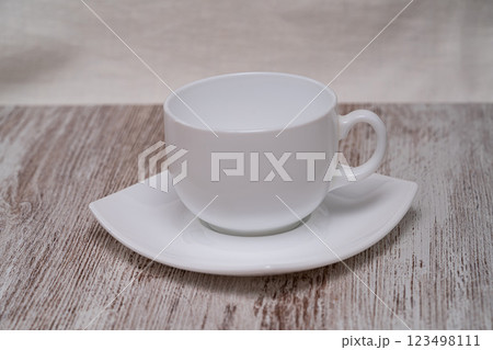 A minimalistic white cup and saucer are elegantly placed on a textured wooden surface, highlighting simplicity and sophistication in design. 123498111