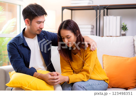 Young asian caring man comforts sad woman with gentle embrace sitting on sofa in living room. Young asian caring man comforts sad woman with gentle embrace sitting on sofa in living room. 123498351