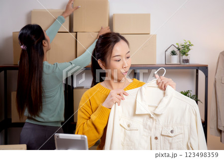 Two young asian woman live online clothing store while showing clothing with tablet on social. Two young asian woman live online clothing store while showing clothing with tablet on social. 123498359
