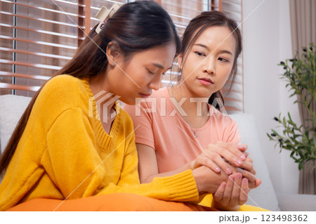 Young asian woman comforting friend with crying and depression sitting on sofa in living room. 123498362