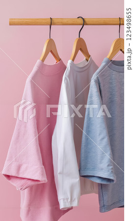 Three shirts hanging on a wooden hanger against a pink background 123498655
