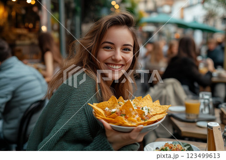 Happy young woman eating nachos at an outdoor restaurant 123499613