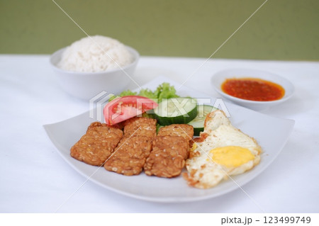 Fried tempeh cutlet with rice and fried egg on white plate 123499749