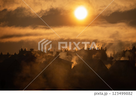 Golden sunrise over village rooftops with smoke rising from multiple chimneys 123499882