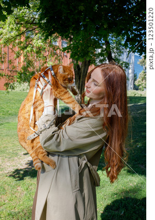 Ginger girl walking a ginger cat on a leash in the park 123501220