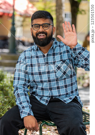 Indian man smiling friendly at camera, waving hands hello, hi, greeting or goodbye in city street Indian man smiling friendly at camera, waving hands hello, hi, greeting or goodbye in city street 123501550