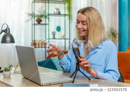 Happy blogger woman recording podcast at table giving workshop webinar speaking at microphone laptop 123501578