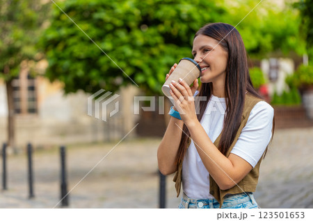 Happy Caucasian young pretty woman enjoying morning coffee hot drink and walking on city street Happy Caucasian young pretty woman enjoying morning coffee hot drink and walking on city street 123501653