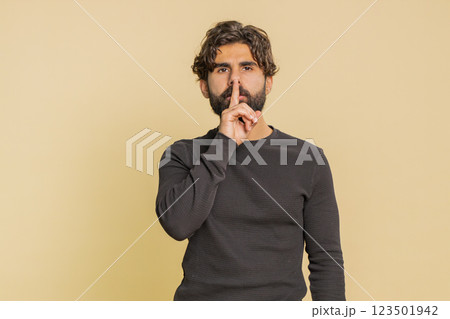 Young Lebanese man presses index finger to lips makes silence gesture over beige studio background 123501942