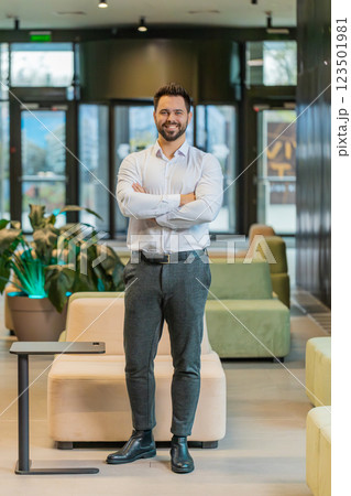 Portrait of happy young businessman with arms crossed looking at camera in modern office hotel lobby Portrait of happy young businessman with arms crossed looking at camera in modern office hotel lobby 123501981