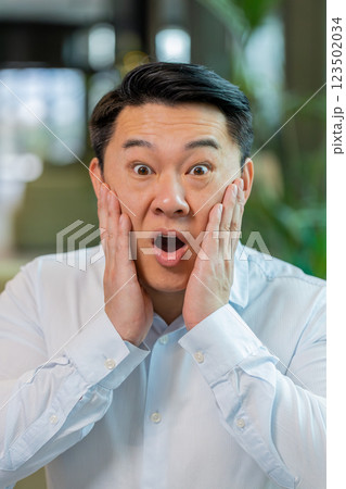 Chinese young businessman in shirt looking at camera shocked by sudden victory in office lobby Chinese young businessman in shirt looking at camera shocked by sudden victory in office lobby 123502034