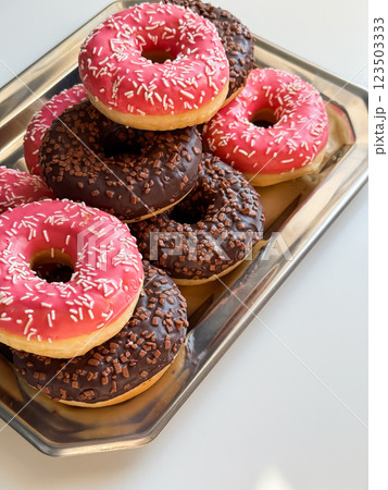 Many pink and brown donuts on metal tray close up Many pink and brown donuts on metal tray close up 123503333