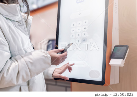 Order via the self-service screen in a cafe and pay by credit card. The woman enters her phone number into the touch menu of the screen on the terminal to pay for the order and have a receipt sent to 123503822