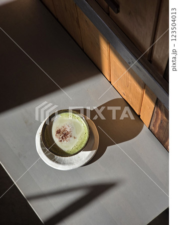 beautifully crafted matcha latte sits on minimalist table, casting soft shadow. warm tones of wood and creamy texture create cozy atmosphere beautifully crafted matcha latte sits on minimalist table, casting soft shadow. warm tones of wood and creamy texture create cozy atmosphere 123504013