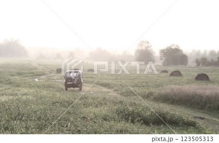Jeep Driving Through Misty Field with Hay Bales 123505313