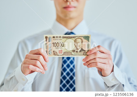 一万円札を持つ20代の若い男性 123506136