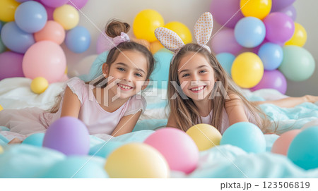 Two girls enjoy a festive celebration with pastel balloons and colorful eggs in a bright setting 123506819