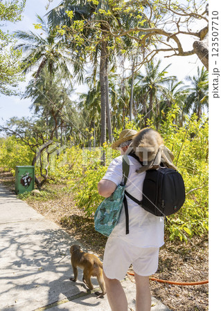 A monkey sits on a man's shoulder and tries to get into his bag. Another monkey walks in front of the man. Monkey Island in Vietnam, Nha Trang. Close-up, selective focus. A monkey sits on a man's shoulder and tries to get into his bag. Another monkey walks in front of the man. Monkey Island in Vietnam, Nha Trang. Close-up, selective focus. 123507710