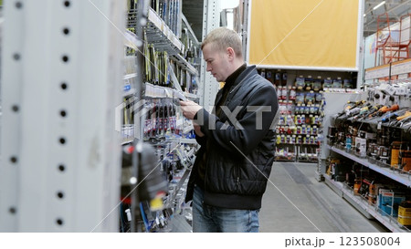 Shopper carefully compares product labels in a home improvement store aisle. A man in a hardware store choosing a tool. Shopper carefully compares product labels in a home improvement store aisle. A man in a hardware store choosing a tool. 123508004